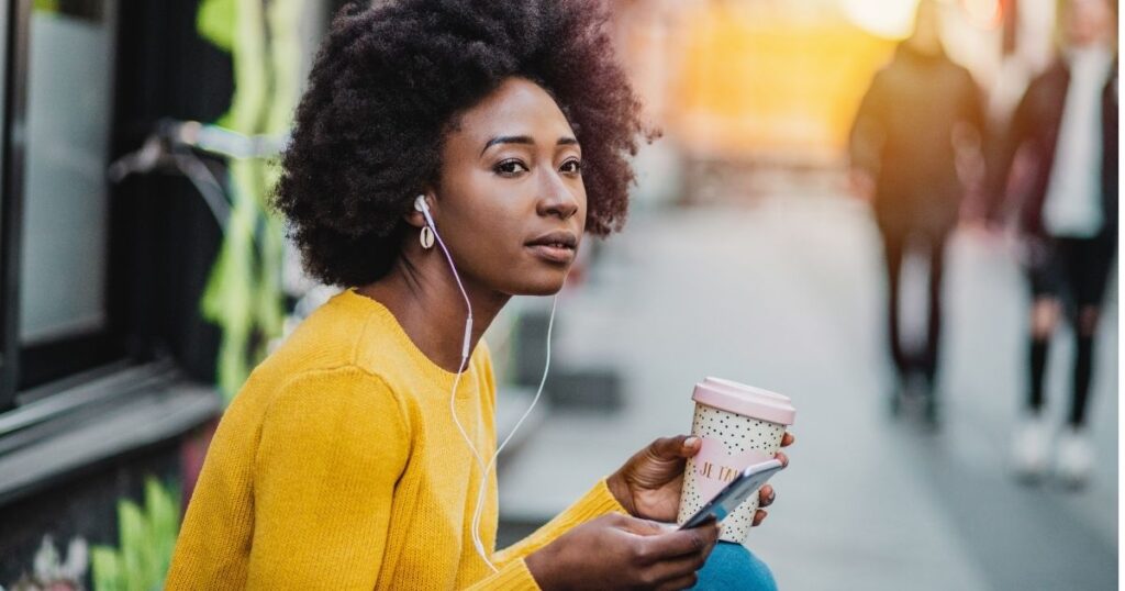 african american woman outside with earbuds and mobile phone