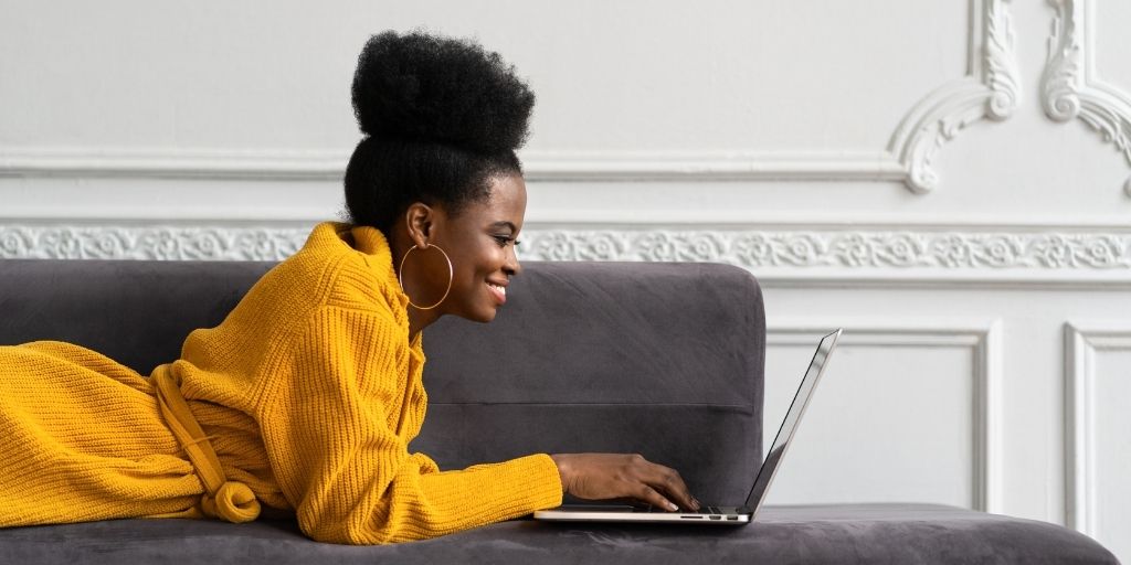 african american woman working on laptop while reclining on luxury chase against minimalst white wall