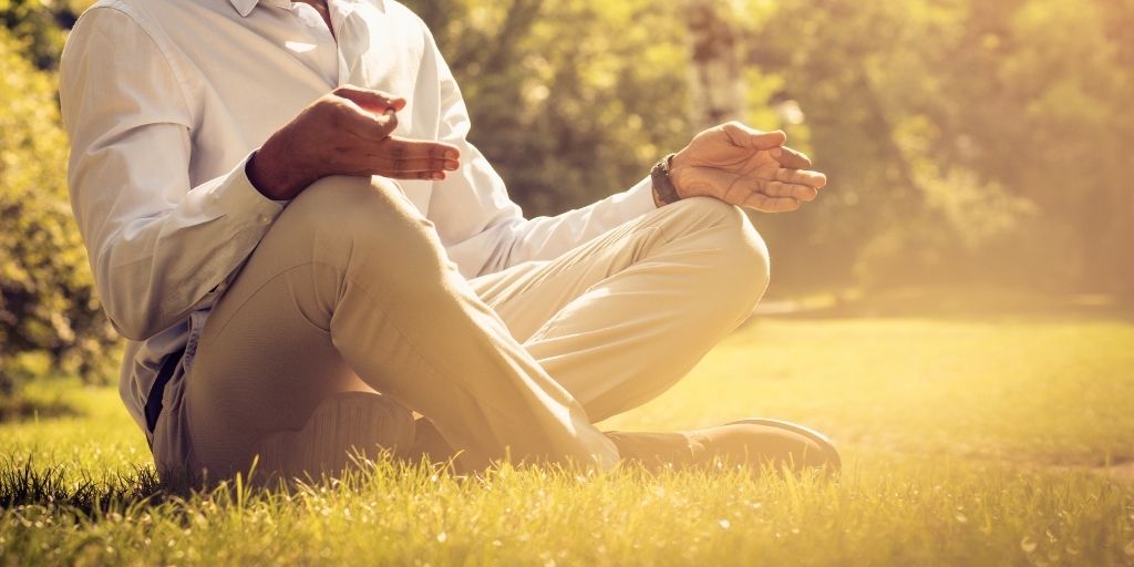 person sitting in grass on a sunny day practicing mindfulness meditation