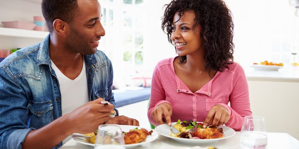 african american couple smiling while eating a healthy meal in kitchen